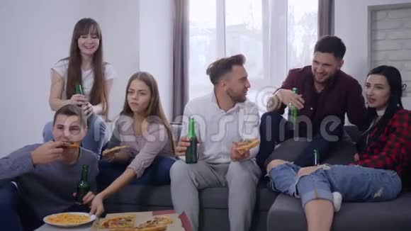 周末在沙发上举行聚会青年朋友们在电视上看电影时喝啤酒吃披萨视频的预览图