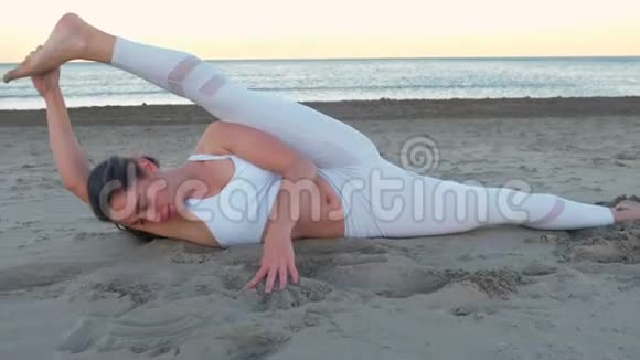 年轻女子在日出时在沙滩上做瑜伽在沙滩上做侧收缩腿视频的预览图