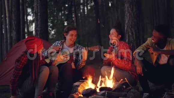 电影中的循环年轻的游客正在弹吉他而他的朋友在唱歌和笑着坐在一起视频的预览图