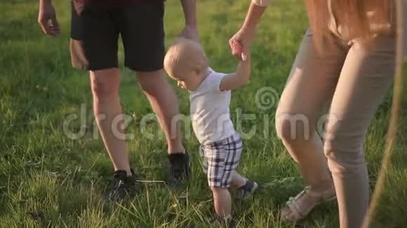 年轻的一家人正在散步手牵着第一个小婴儿在绿色公园里视频的预览图