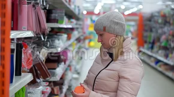 一位戴着帽子和羽绒服的中年妇女在超市里选择了一个红色的热水瓶视频的预览图