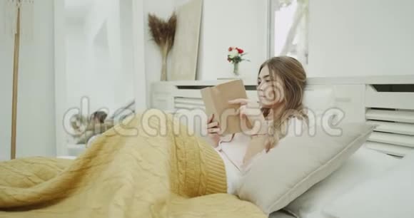 早上舒适的卧室里一位漂亮的女士在读一本书对她的男人在床上吃早餐感到惊讶视频的预览图
