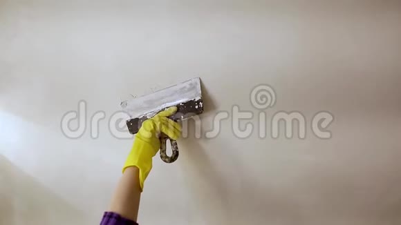 工人手戴黄色手套手拿腻子刀用抹子在白色墙壁上用石膏或腻子修补一个洞翻修视频的预览图