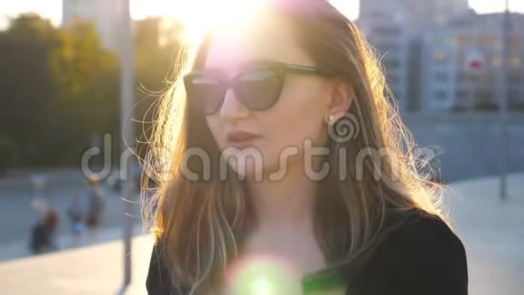 年轻女商人戴着太阳镜在城市街道上行走的肖像背景是太阳耀斑漂亮的脸视频的预览图