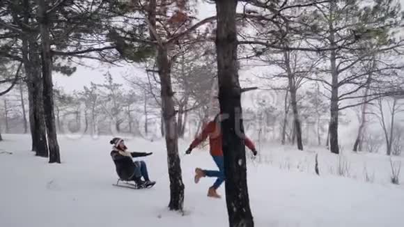 可爱的夫妇在下雪的冬天滑雪下雪时男人和女朋友拉雪橇女人玩得开心视频的预览图