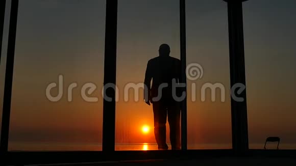 日落时分站在房子玻璃门附近的人视频的预览图
