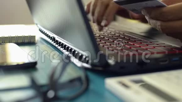 手持信用卡和输入笔记本电脑键盘进行在线支付的人的手视频的预览图