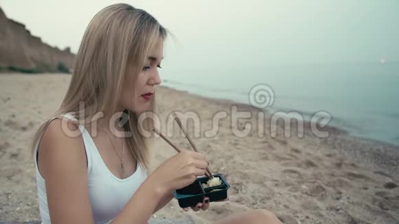 年轻的白种人女孩用传统的日本筷子拿起生姜放进嘴里在沙滩上海岸上视频的预览图
