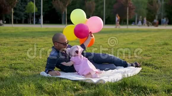 爸爸戴着气球的眼镜小女儿躺在公园的毯子上然后女儿摘下爸爸的眼镜吻他视频的预览图
