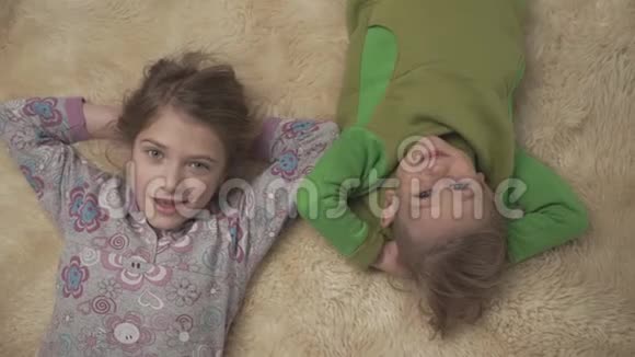 可爱的小孩子穿着睡衣躺在地板上铺着蓬松的地毯兄妹在一起快乐的兄弟姐妹视频的预览图