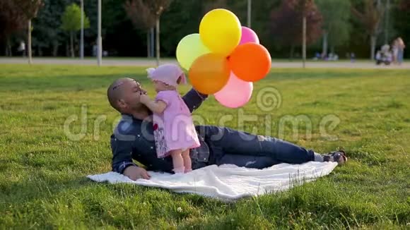 爸爸戴着气球的眼镜小女儿躺在公园的毯子上然后女儿摘下爸爸的眼镜吻他视频的预览图