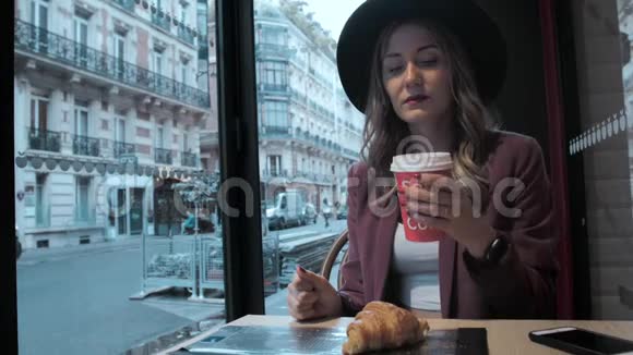 一位戴着帽子的漂亮法国商人正在一家咖啡店里喝咖啡背景是一条法国街视频的预览图