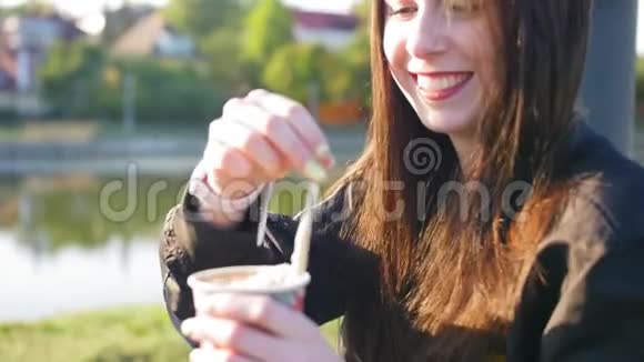 有着黑色长发和红唇的快乐女孩正在喝咖啡在背景池塘里近距离射击视频的预览图