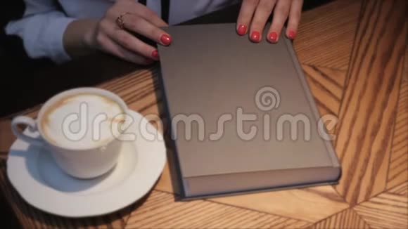 这段视频讲述的是年轻女子在舒适的咖啡馆里一边喝咖啡一边打开和看书视频的预览图