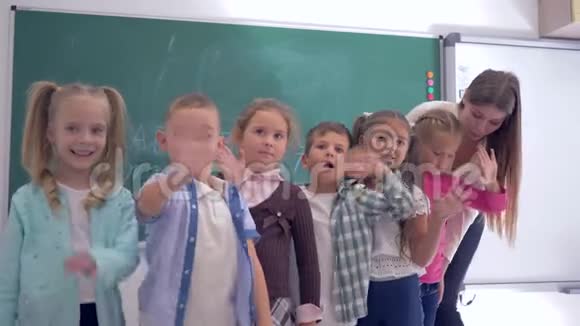 小学一组幼儿带着幼儿教师在教室的黑板背景上挥手视频的预览图