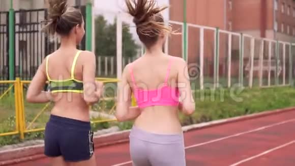 两个漂亮年轻女人的肖像他们在夏季体育场跑步一个戴着耳机听音乐后景视频的预览图