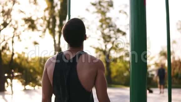 强壮的肌肉男穿着黑色衬衫在地平线上艰难地拉起在运动场上树木和阳光照耀着视频的预览图