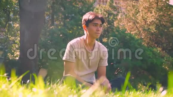 梦想中的亚洲男孩独自在公园里闲逛坐在阳光下的草地上清新的春天气氛视频的预览图