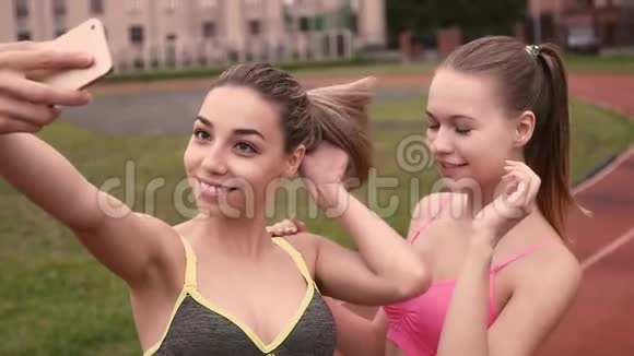 两个女孩在用电话拍照时做鬼脸年轻的健身女性在公园拍照时摆姿势视频的预览图