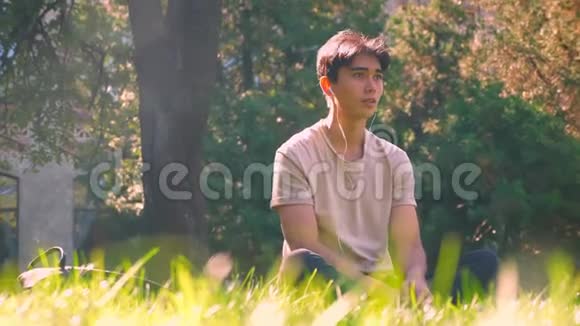 安静的亚洲人坐在树下的绿草上听着音乐纯净的自然在大城市的匆忙中视频的预览图