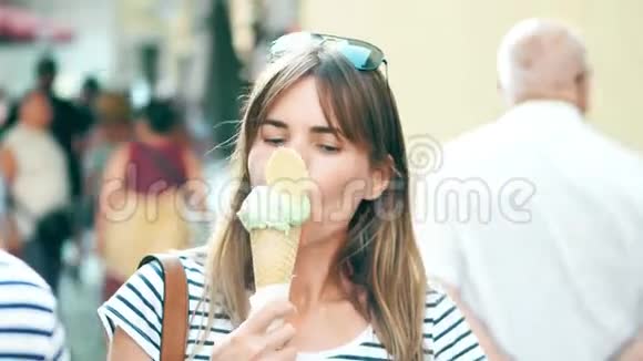 年轻的美女吃着冰淇淋筒沿着蹲伏的旅游街散步视频的预览图