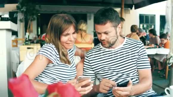 年轻的幸福夫妇在咖啡馆里用智能手机看照片视频的预览图