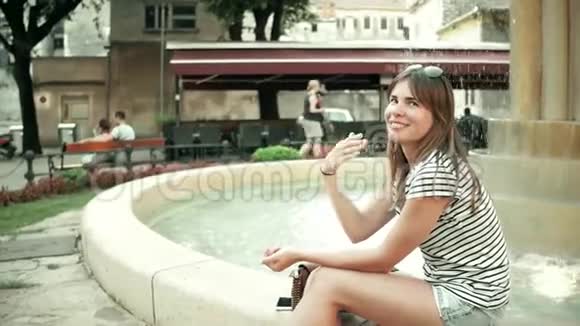 坐在街边喷泉边的漂亮年轻女子视频的预览图