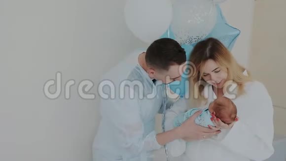 妈妈抱着熟睡的新生宝宝快乐的年轻父母亲吻孩子视频的预览图