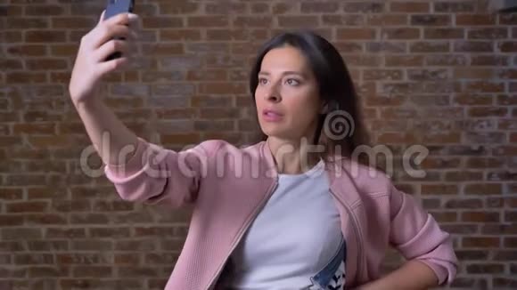 漂亮的白种人女性正在为自己拍照一边看着手机上的网络摄像机一边穿着红色衣服视频的预览图