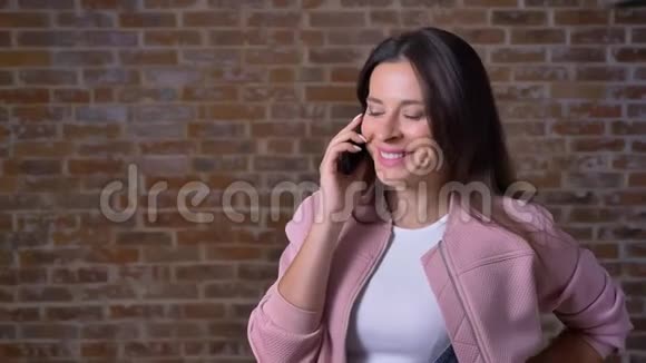 斯迈利漂亮的白种人女人一头乌黑的长发正在电话里情绪化地交谈站在砖背景附近视频的预览图