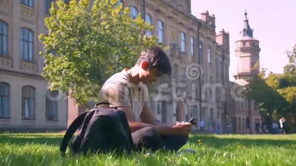 可爱的坐在公园的草地上亚洲人正在使用他的智能手机用相机在圆圈上推着微笑着快乐的脸视频的预览图