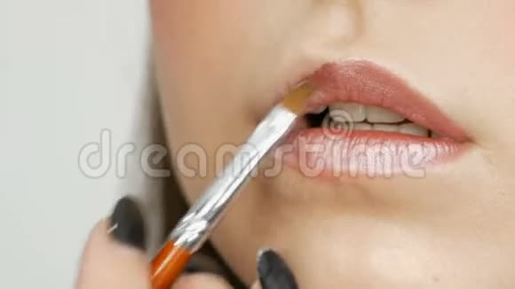 化妆师做化妆女孩模特口红遮光用特殊的刷子涂在嘴唇上近距离观看视频的预览图