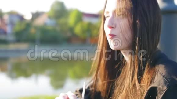 有着黑色长发和红唇的快乐女孩正在喝咖啡在背景池塘里近距离射击视频的预览图