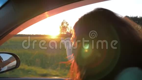 在日落时分快乐的年轻女子在车里在空中嬉戏视频的预览图