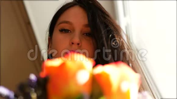 一个漂亮的女孩把一束花送到鼻子上闻着它们站在窗前特写视频的预览图