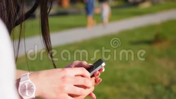 站在公园里的年轻漂亮的夫妇使用现代手机女孩在他的智能手机上视频的预览图