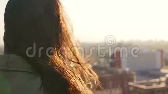 后景风吹长黑发美丽的年轻女人日落时站在屋顶上的女孩慢节奏视频的预览图
