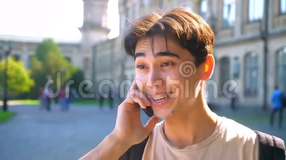 漂亮的亚洲男孩正在打电话微笑着说话阳光明媚城市景色为背景视频的预览图