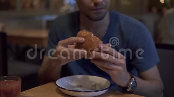 一个穿蓝色T恤的黑发男人在咖啡馆里吃汉堡晚餐吃着美味的汉堡双手捧着模糊的视频的预览图