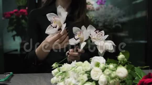 专业的花艺师在一家花店工作为花束准备兰花兰花和白玫瑰女人的手紧紧视频的预览图