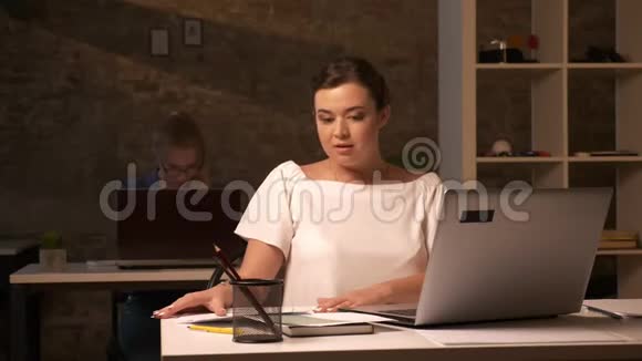 专注思考的面孔集中在白种人的商业女孩她正在协调她的文件坐在工作场所与笔记本电脑视频的预览图