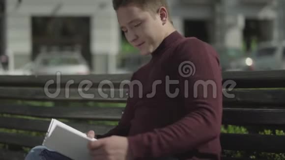年轻人在一条城市街道的长凳上看书视频的预览图