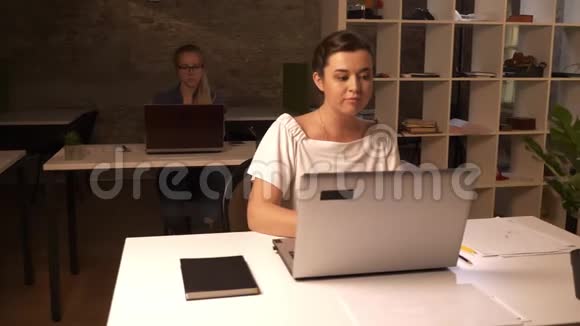 美丽的白种人同事女孩坐在笔记本电脑前打字专注工作情绪办公室砖视频的预览图
