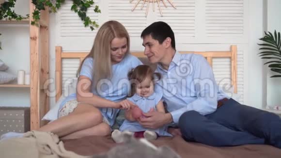 微笑的家人在床上爸爸和妈妈和他们的小女儿玩玩具视频的预览图