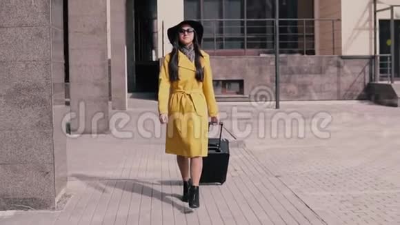 穿着黄色雨衣帽和眼镜的时髦女孩带着行李微笑着视频的预览图