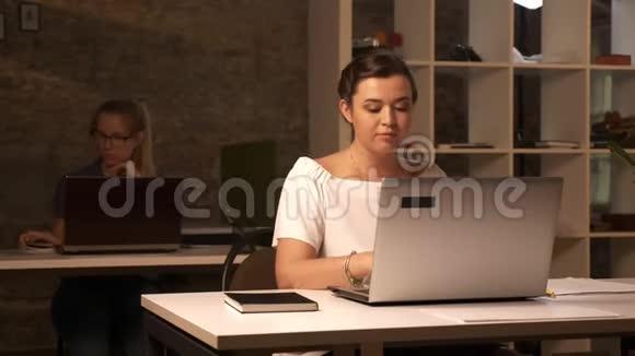 两位白种人的女商人坐在一个又一个的室内笔记本电脑上在一间砖褐色的工作室里工作视频的预览图