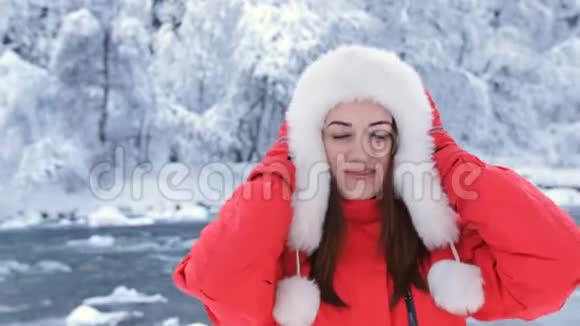 一位穿着红色夹克和帽子的美女在河边洞穴附近的树林里的特写肖像视频的预览图