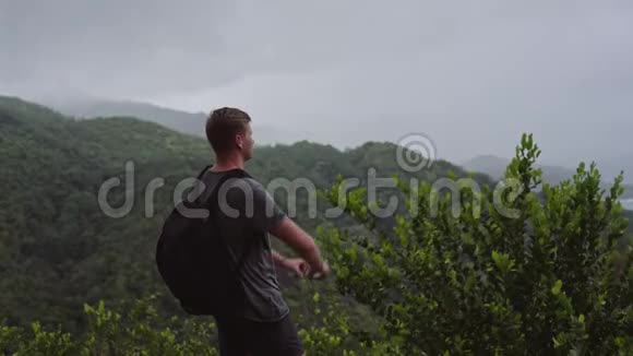 一个背着背包的旅行者站在山顶在他的手机上拍摄一幅风景视频的预览图