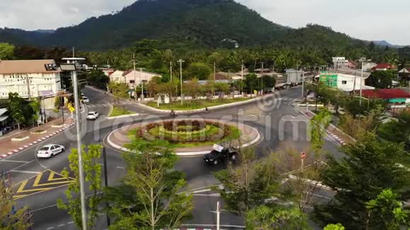 在丛林附近的小镇上汽车在环形交叉路口上行驶车辆行驶在主干道中间的环形交叉路口视频的预览图