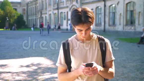 一个微笑的亚洲男人正在大街上阳光下和他身后的宏伟建筑上滚动着他的手机视频的预览图